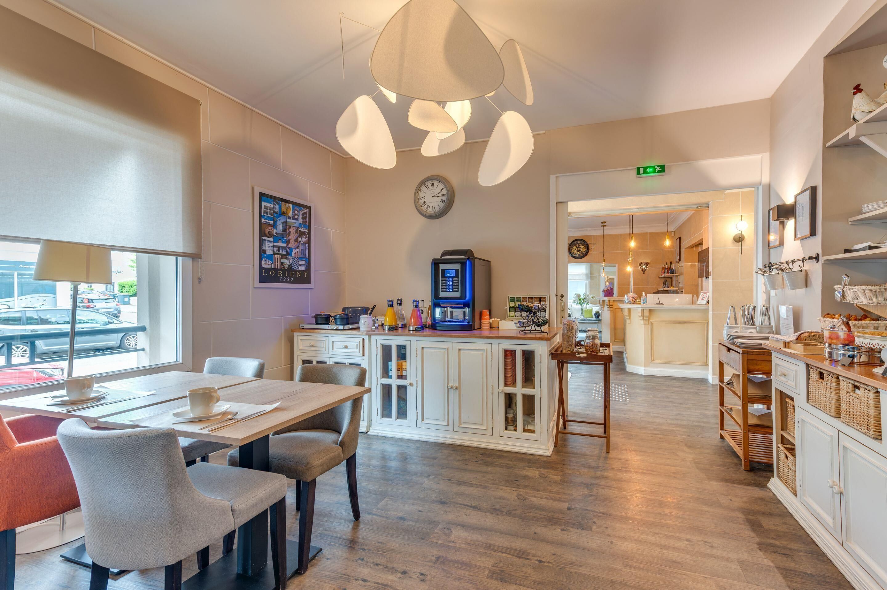 A modern kitchen with a dining area, equipped with a coffee machine, a clock, and a view of the street outside.