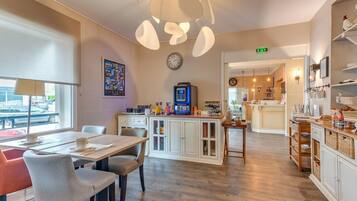 A modern kitchen with a dining area, equipped with a coffee machine, a clock, and a view of the street outside.