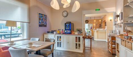 A modern kitchen with a dining area, equipped with a coffee machine, a clock, and a view of the street outside.