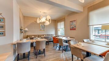 Un espace de restauration moderne, doté de plusieurs tables et chaises, d’un luminaire central et d’œuvres d’art accrochées aux murs.
