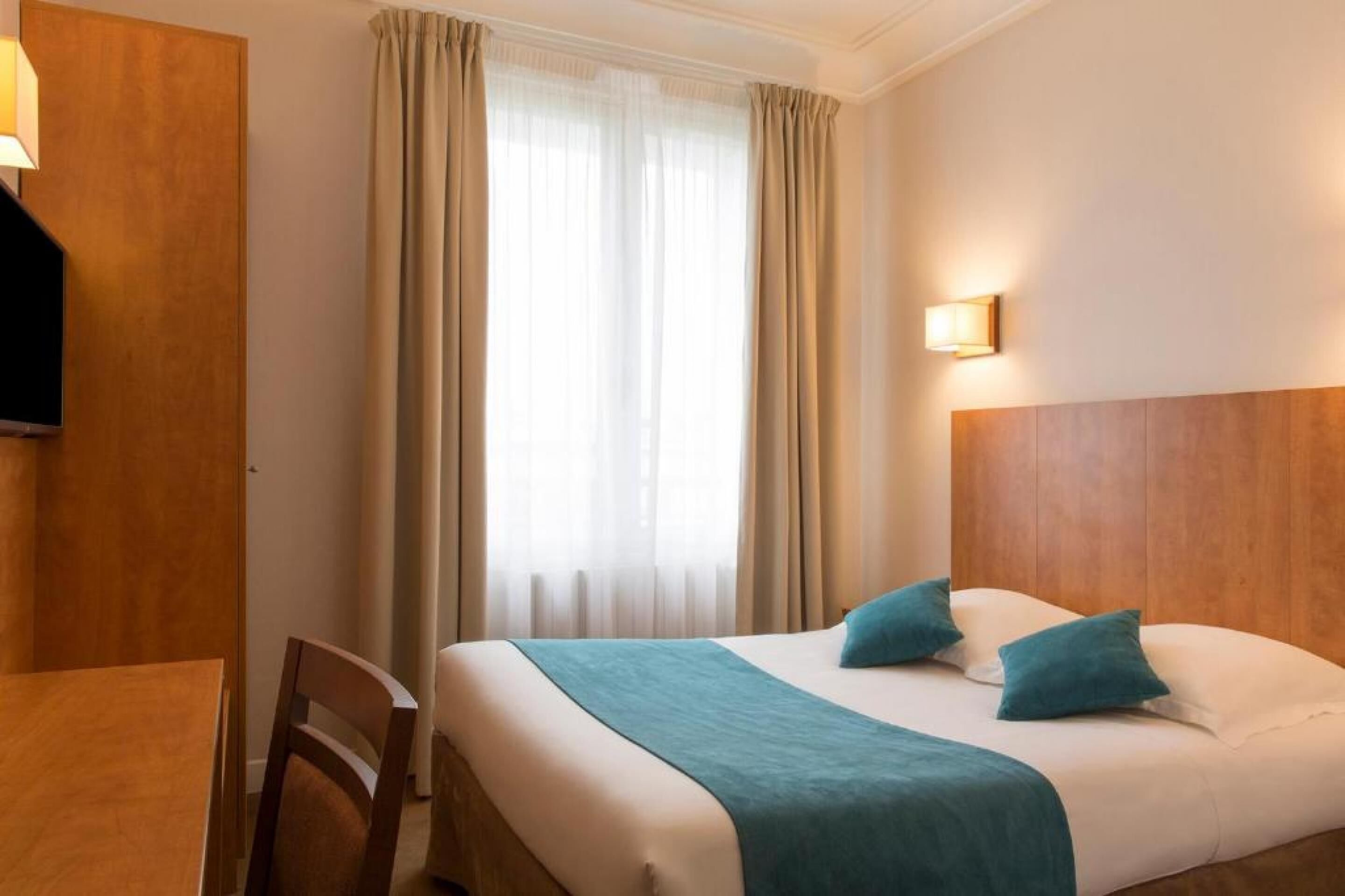 Habitación de hotel con cama, dos almohadas, mesita de noche, silla, escritorio y televisor.