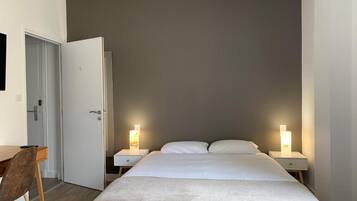 Une chambre à coucher avec un lit, deux tables de chevet avec des lampes, une chaise en bois et une porte.