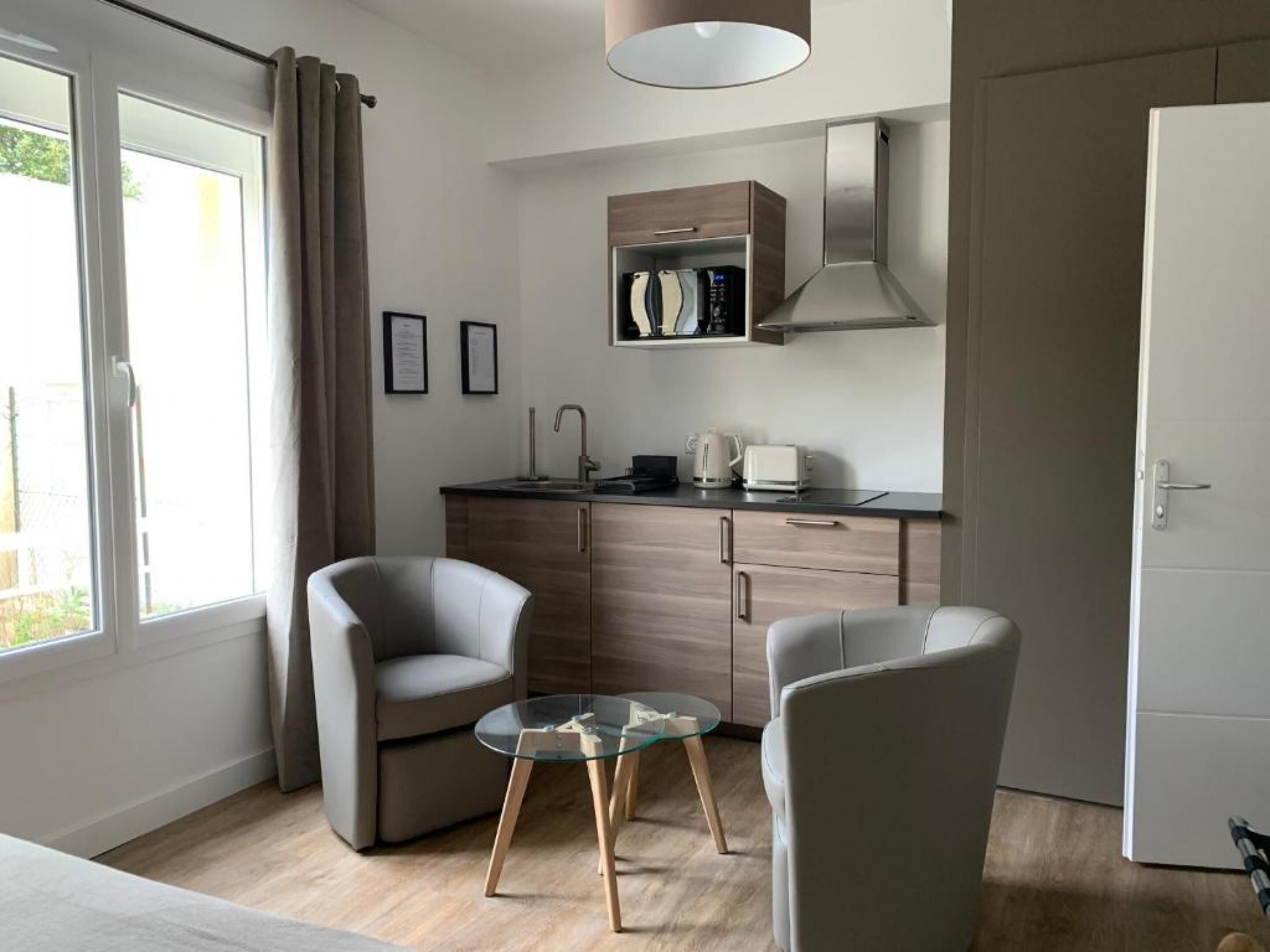A modern kitchen with a built-in oven, a coffee maker, and a toaster. There are two chairs and a glass table in the living area.