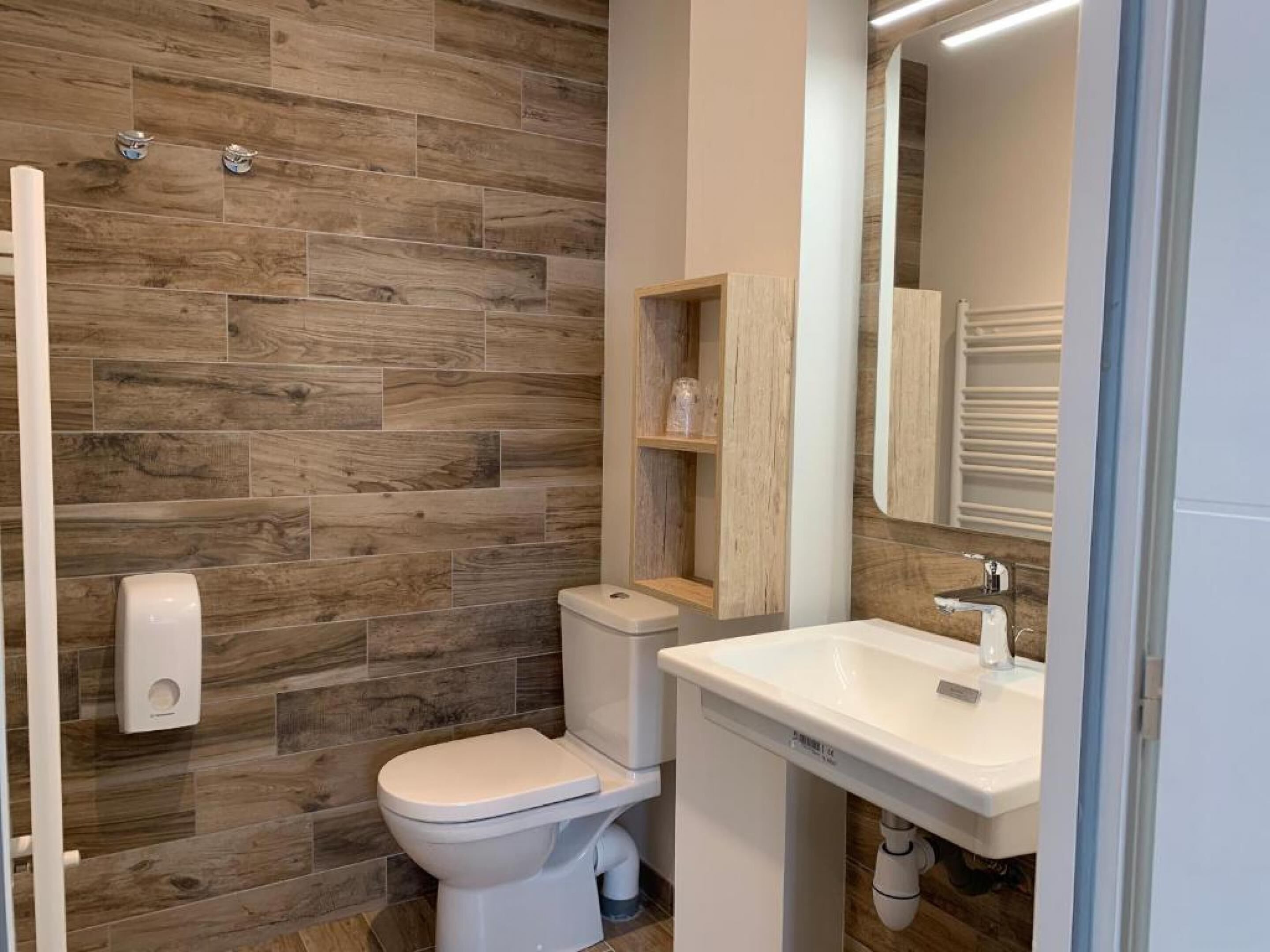 Une salle de bain moderne avec un mur en bois, des toilettes, un lavabo et un miroir.