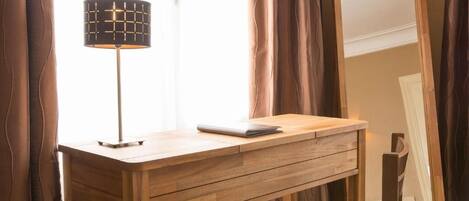 Una scrivania in legno con una lampada, uno specchio e una sedia in una stanza con tende.
