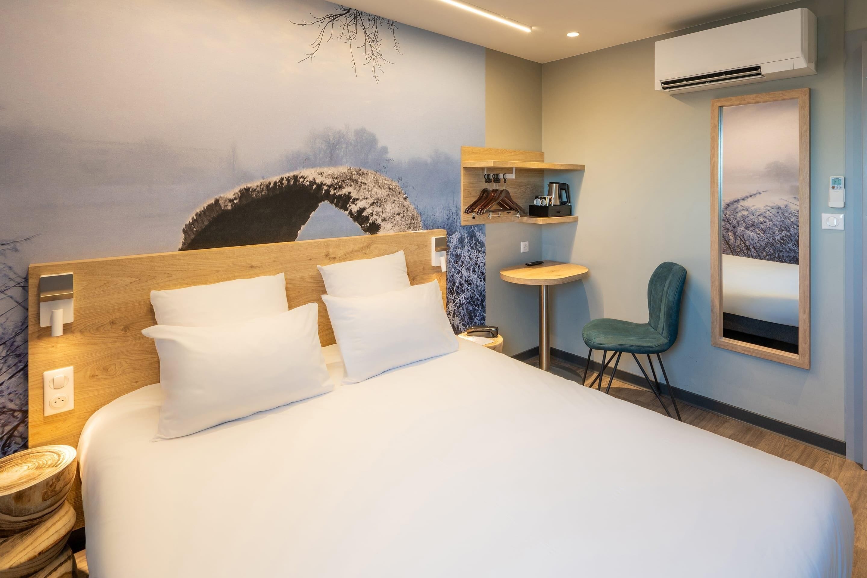 Una habitación de hotel moderna con una cama grande, una mesita redonda pequeña, una silla y un aire acondicionado de pared.