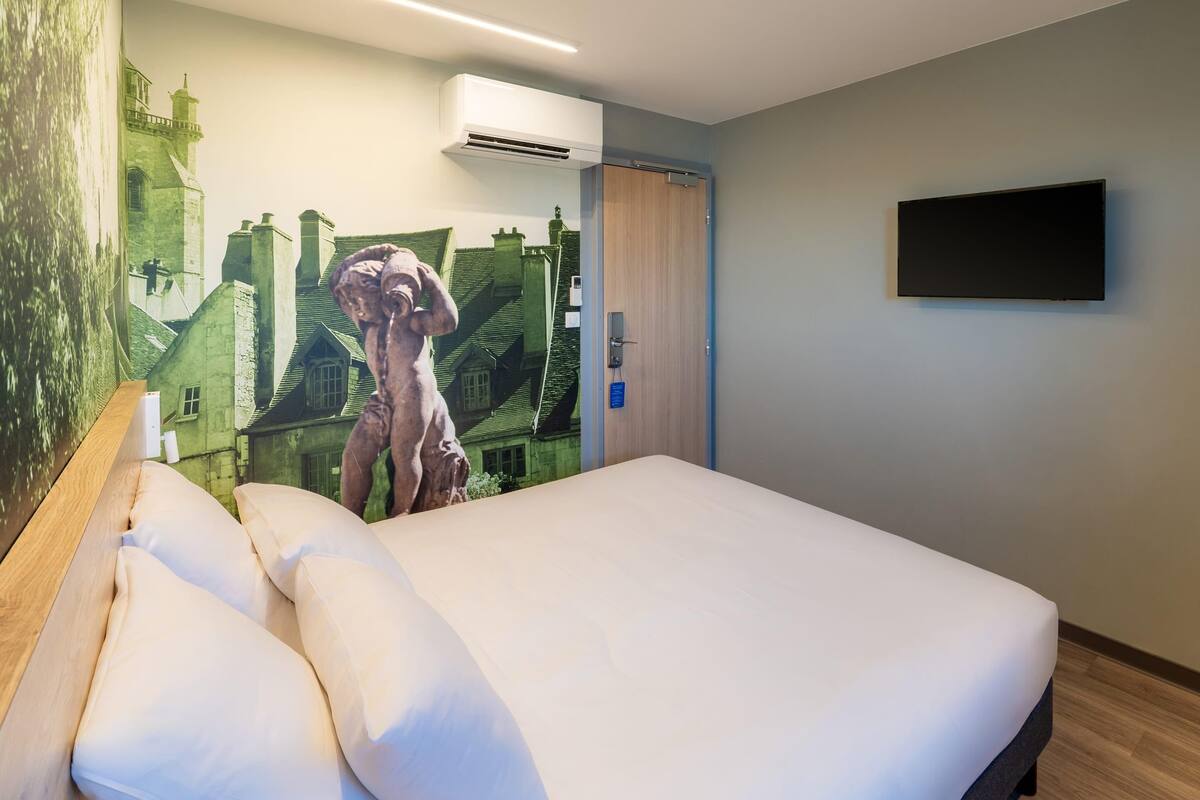 A hotel room with a bed, a wall-mounted TV, and a mural of a castle.