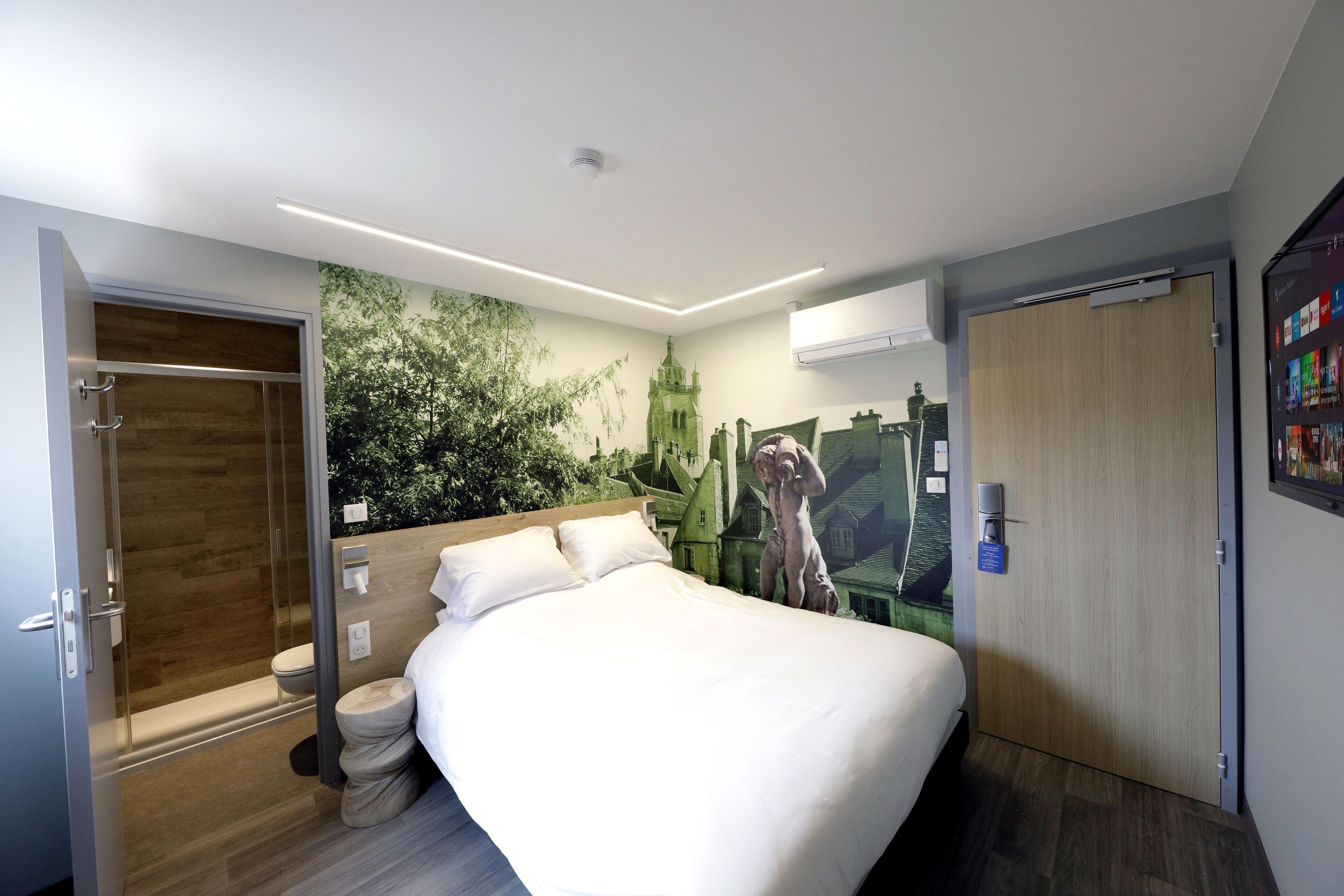 A modern hotel room with a large bed, a shower area, and a mural of a castle.
