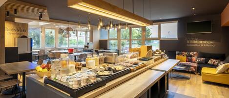 A modern café with a long counter displaying various food items and a seating area with a sofa and chairs.