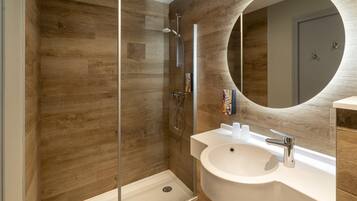 Un baño moderno con pared de madera, ducha con cerramiento de vidrio, lavamanos blanco y espejo redondo.