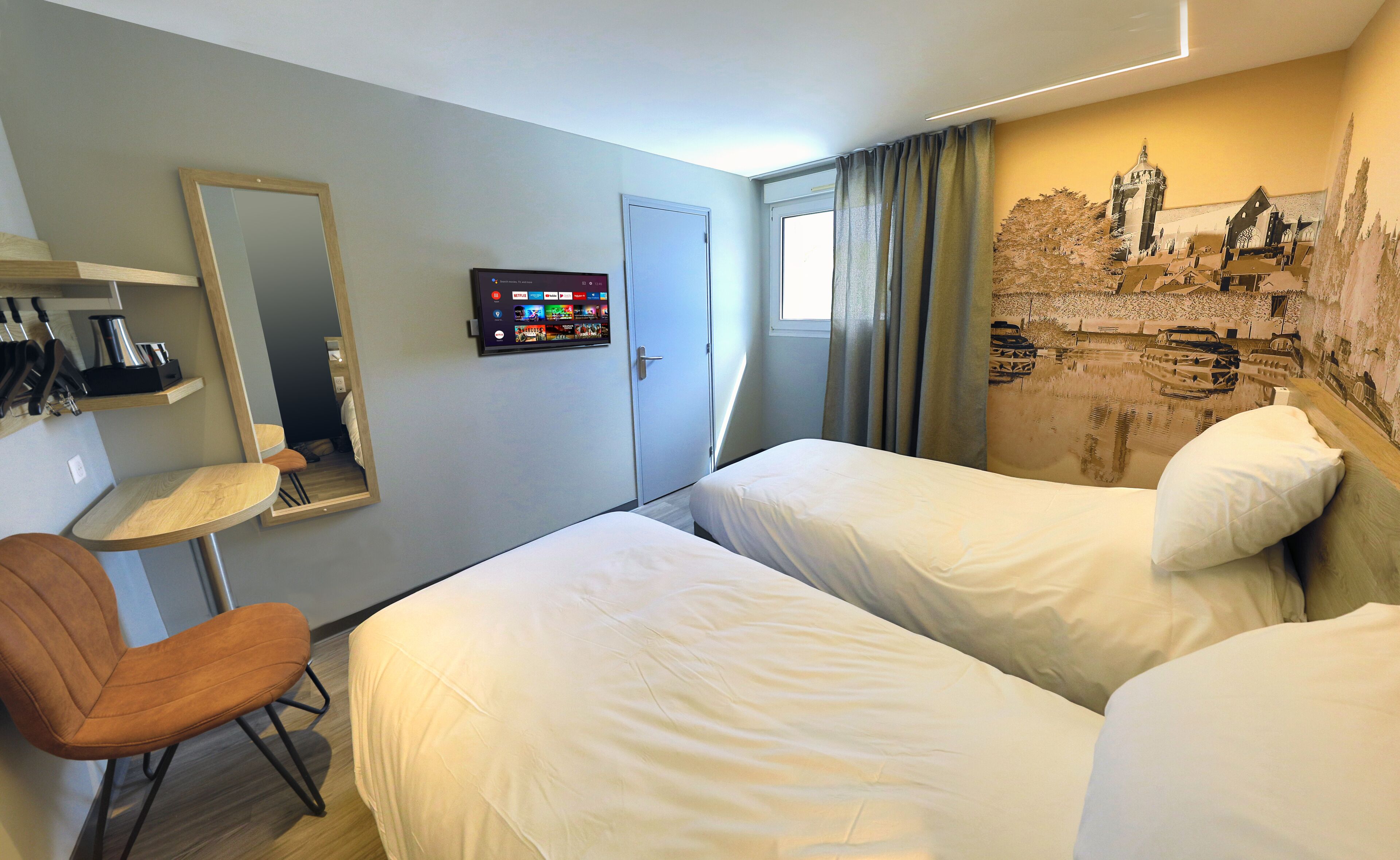 Habitación de hotel con dos camas, un escritorio con silla, un espejo, un televisor y un mural en la pared.