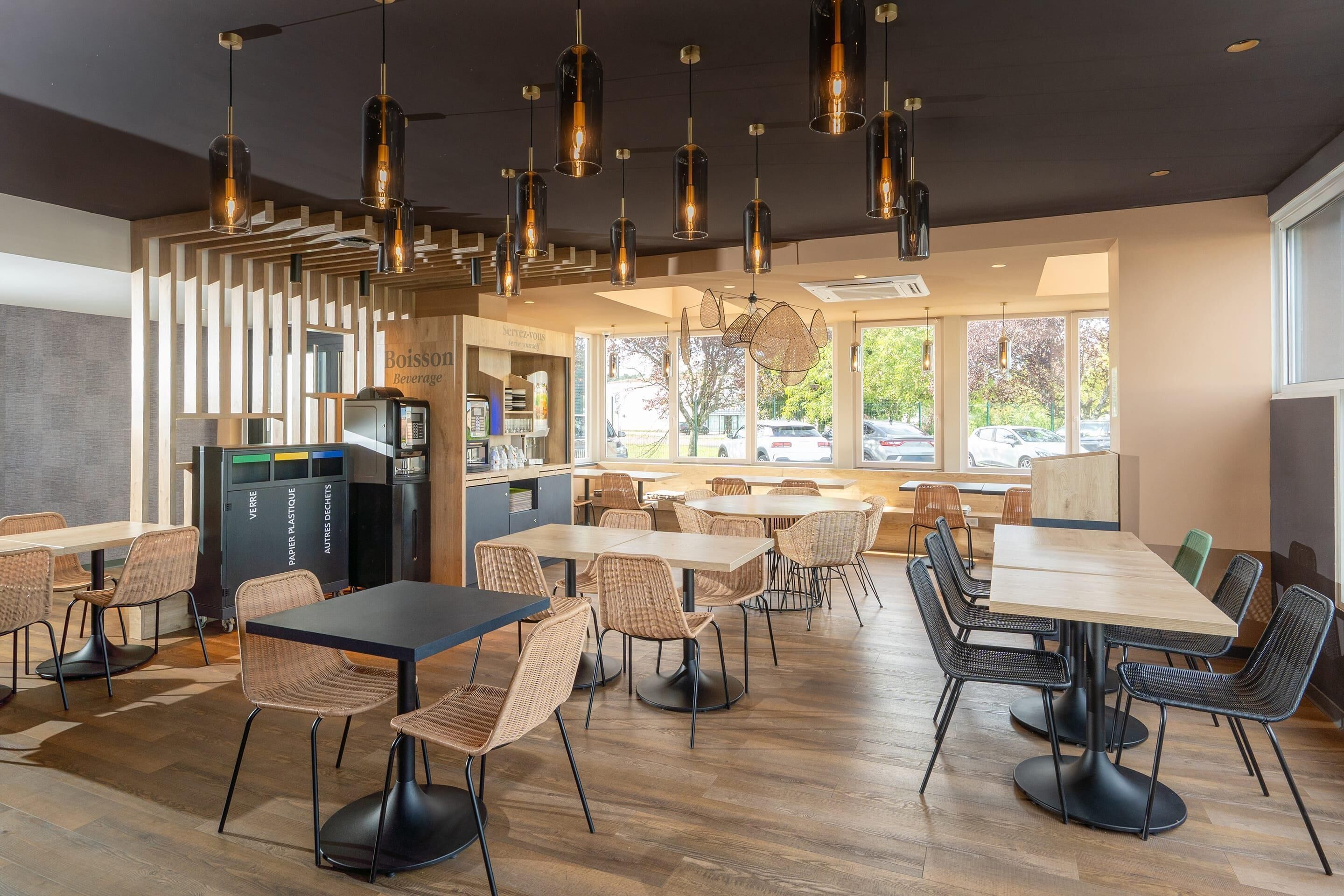 A modern cafe interior with wooden furniture, pendant lighting, and large windows.