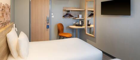 Une chambre d’hôtel avec un lit, une chaise, une petite table, un téléviseur et un miroir.