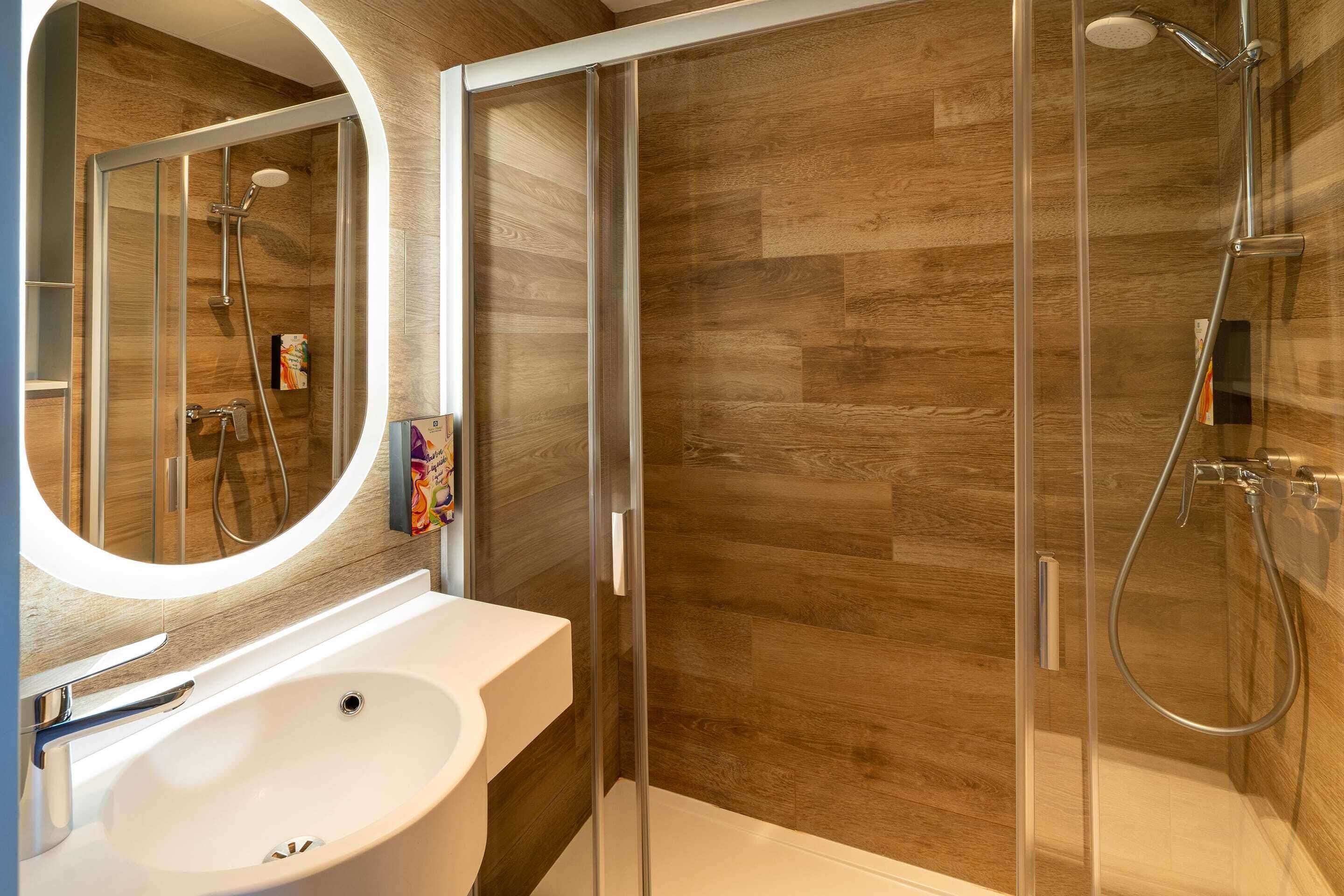 A modern bathroom with a wooden floor, a white sink, and a glass shower enclosure.
