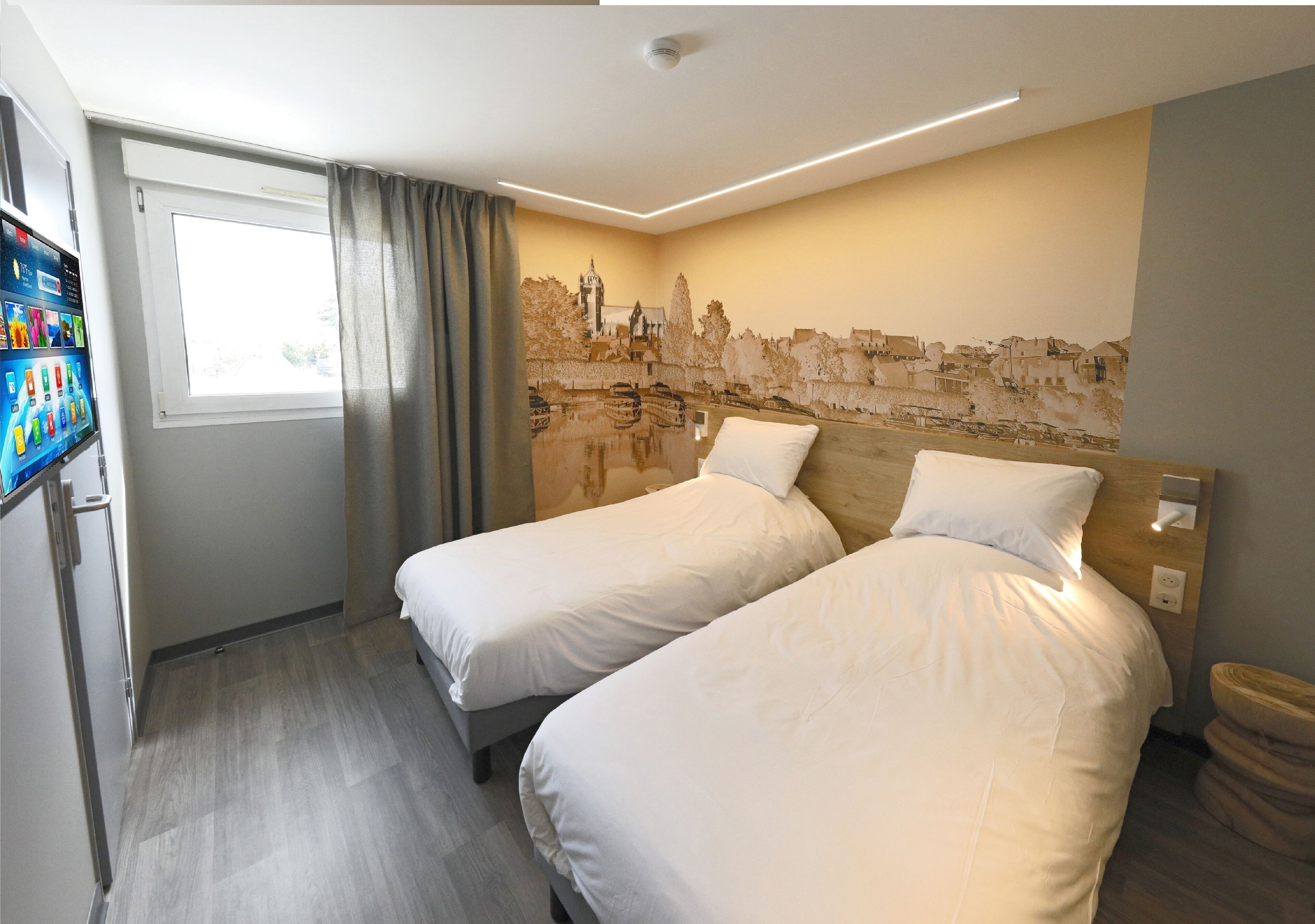 A hotel room with two beds, a window with curtains, a wall mural, and a small trash bin.
