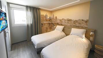 A hotel room with two beds, a window with curtains, a wall mural, and a small trash bin.