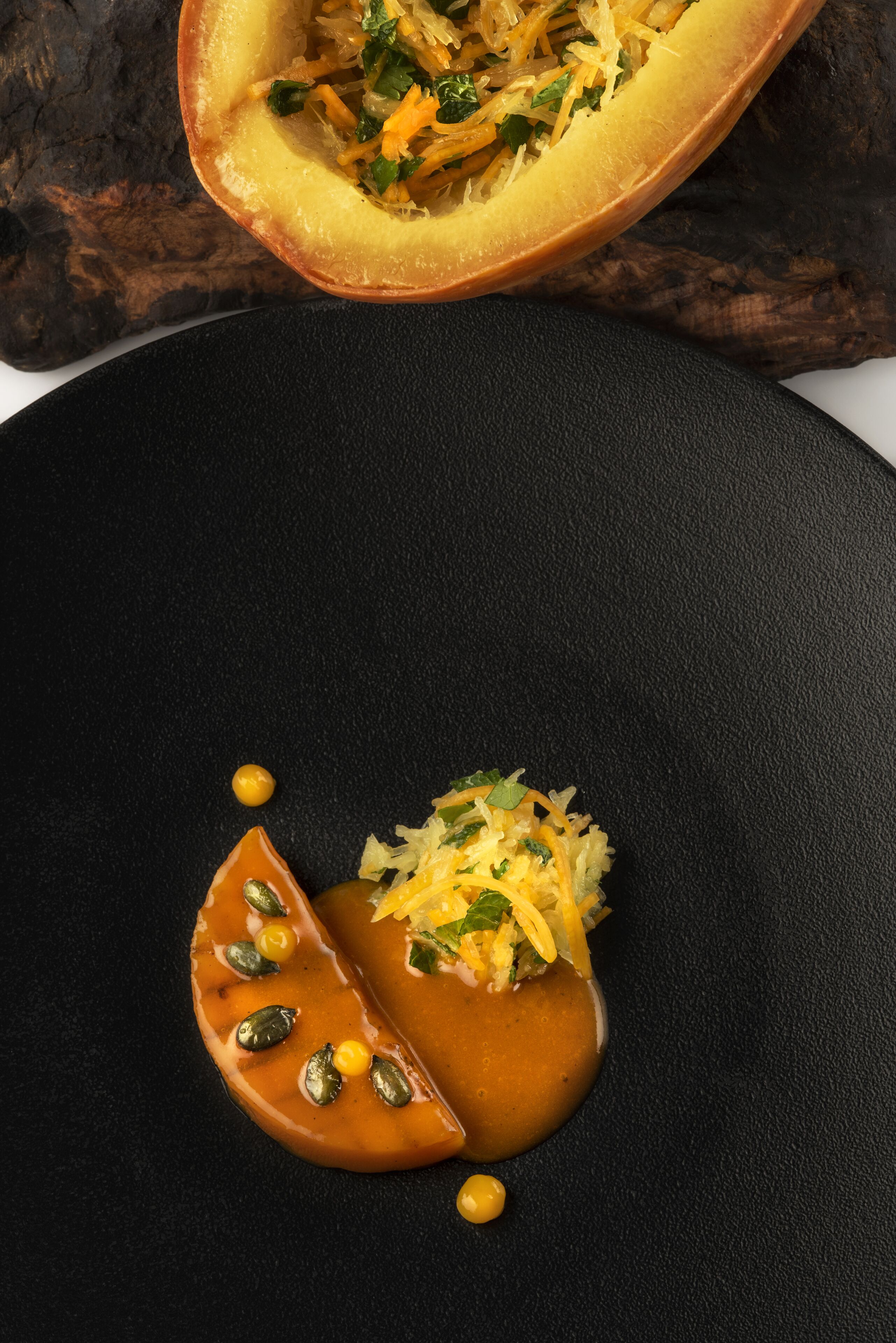 A dessert presentation on a black plate with a pumpkin and a sauce.