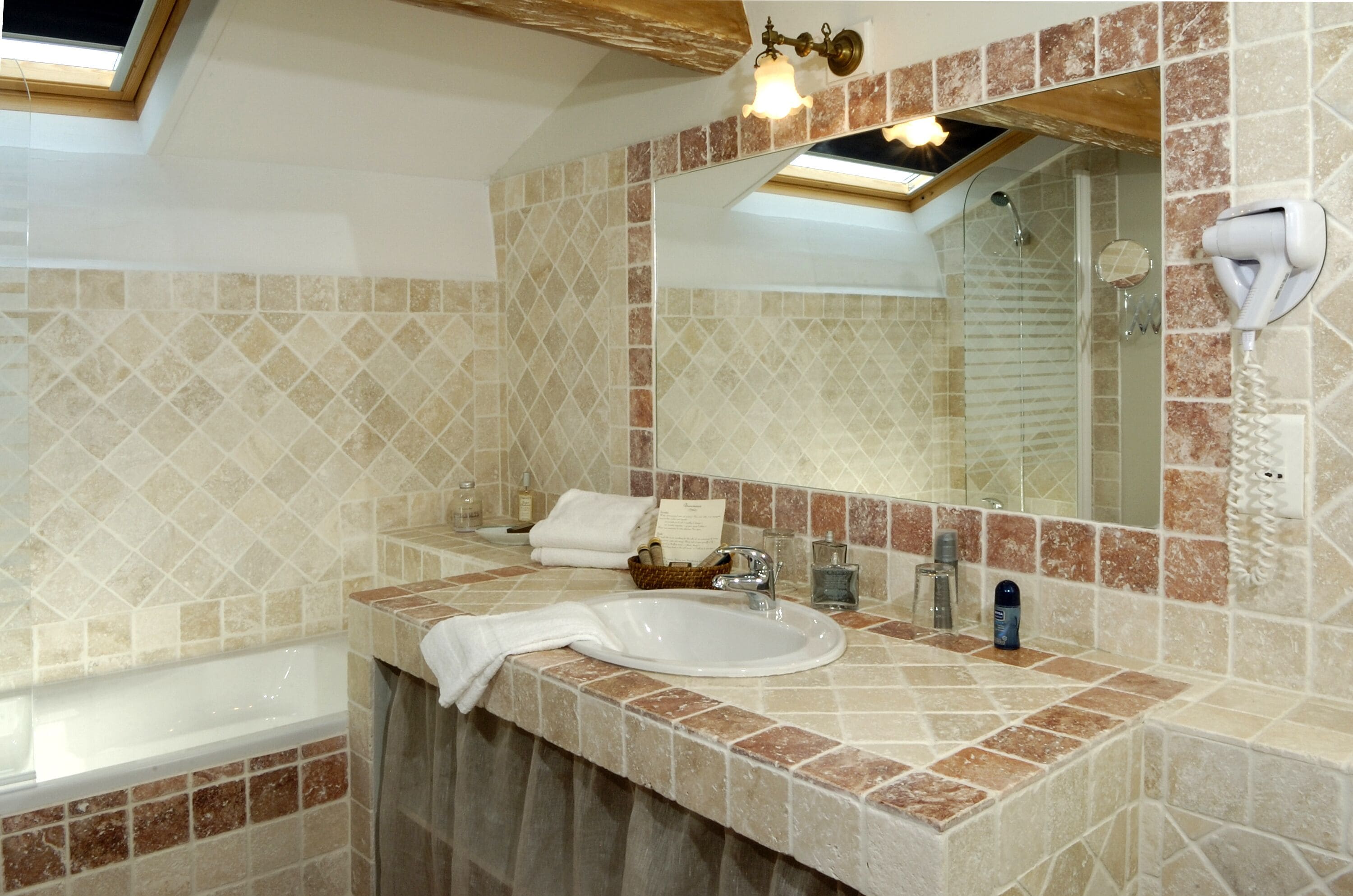 A bathroom with a bathtub, a sink, a mirror, and a hairdryer mounted on the wall.