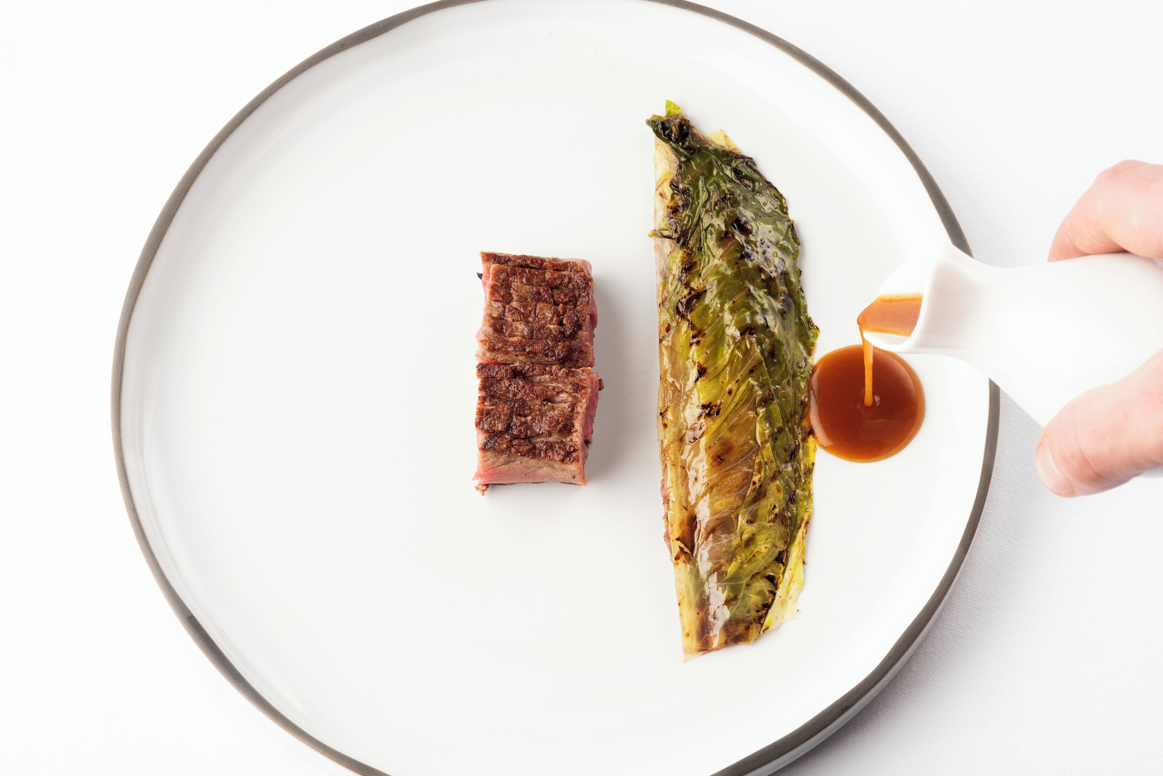 A plate with a piece of meat and a rolled vegetable, with sauce being poured onto it.