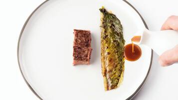 A plate with a piece of meat and a rolled vegetable, with sauce being poured onto it.