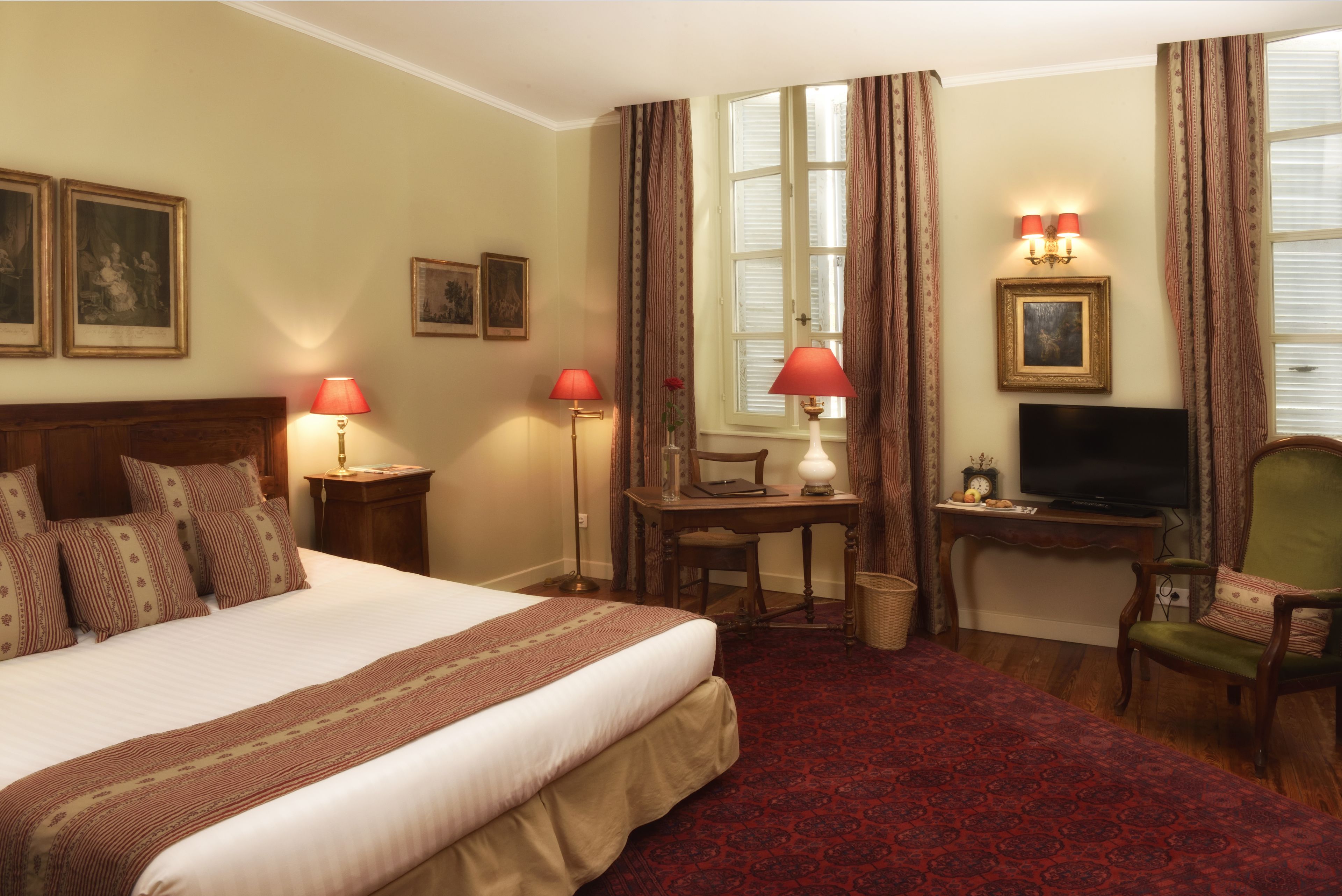 A hotel room with a large bed, two bedside lamps, a desk with a chair, a television, and a window with curtains.