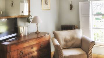 Une pièce comprenant une commode en bois, un fauteuil beige, un tapis à motifs, un miroir et un tableau encadré accroché au mur.