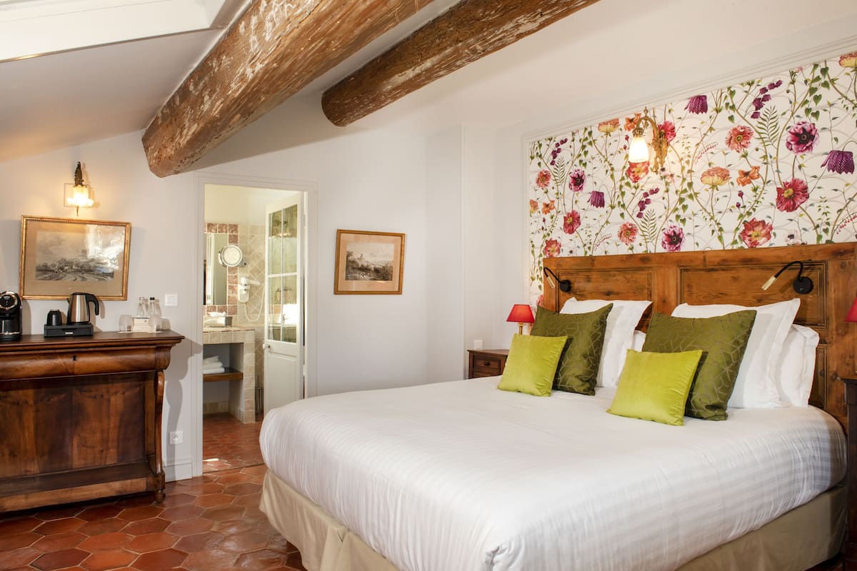 Un dormitorio con una cama grande, cabecera de madera, papel tapiz floral y un aparador de madera.