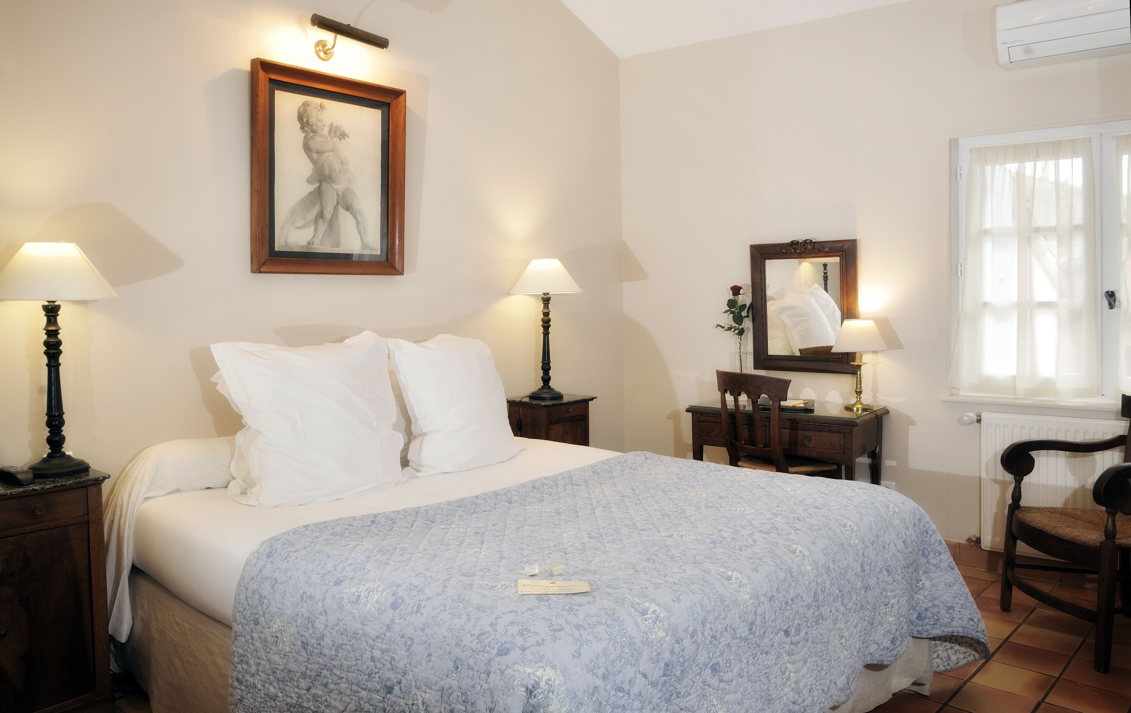 Un dormitorio con una cama, dos mesitas de noche, un tocador, una silla, un espejo y una obra de arte enmarcada en la pared.