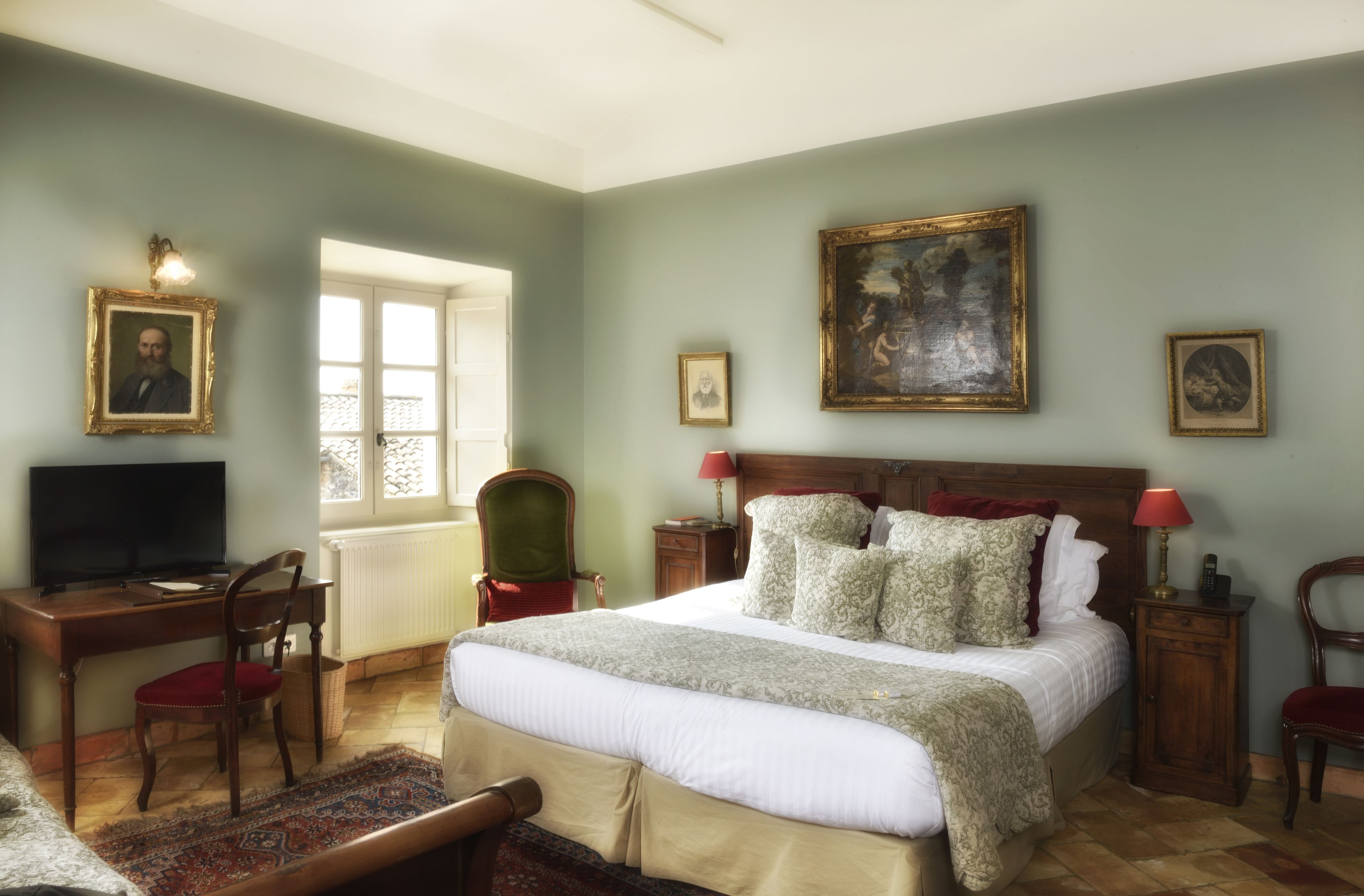 Un dormitorio con cama, escritorio, silla, televisor y cuadros en las paredes.