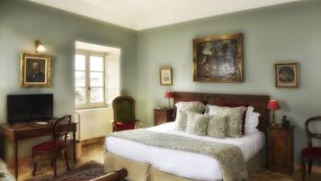 Un dormitorio con cama, escritorio, silla, televisor y cuadros en las paredes.