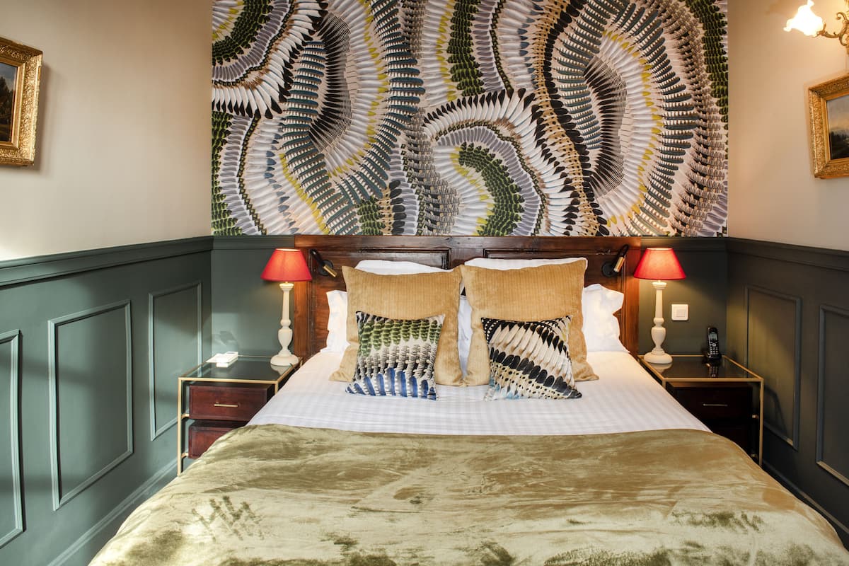 Habitación de hotel con una cama grande, dos mesitas de noche, un teléfono y un adorno decorativo sobre la cama.