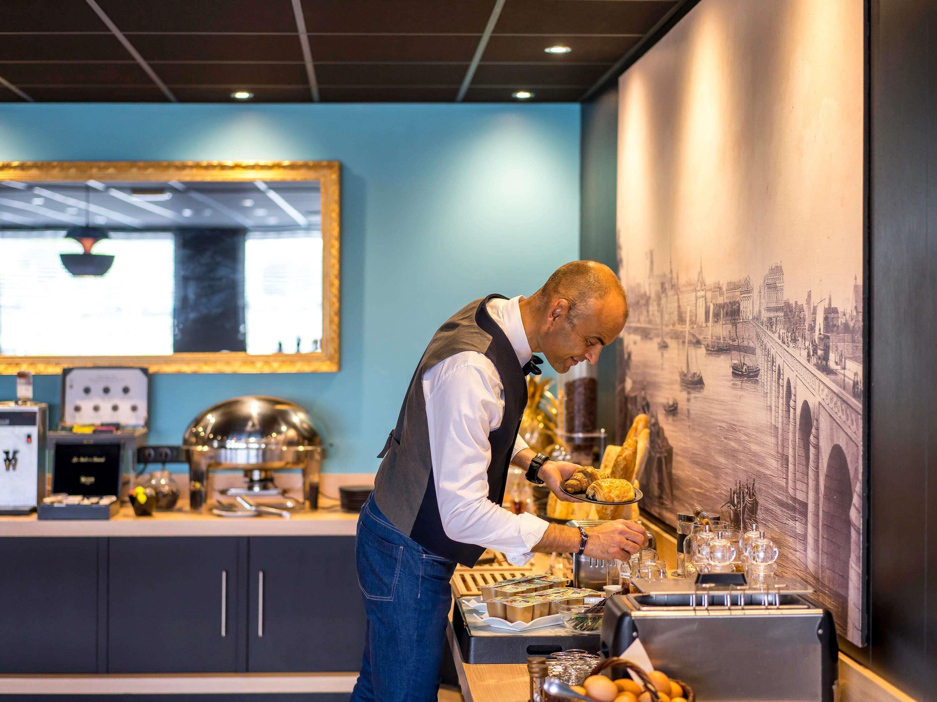 Zona de bar con un bartender preparando bebidas, una barra con diversos alimentos y una gran obra de arte urbana enmarcada en la pared.