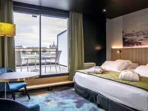 Een hotelkamer met een bed, een stoel, een tafel, uitzicht over de stad en een schilderij aan de muur.