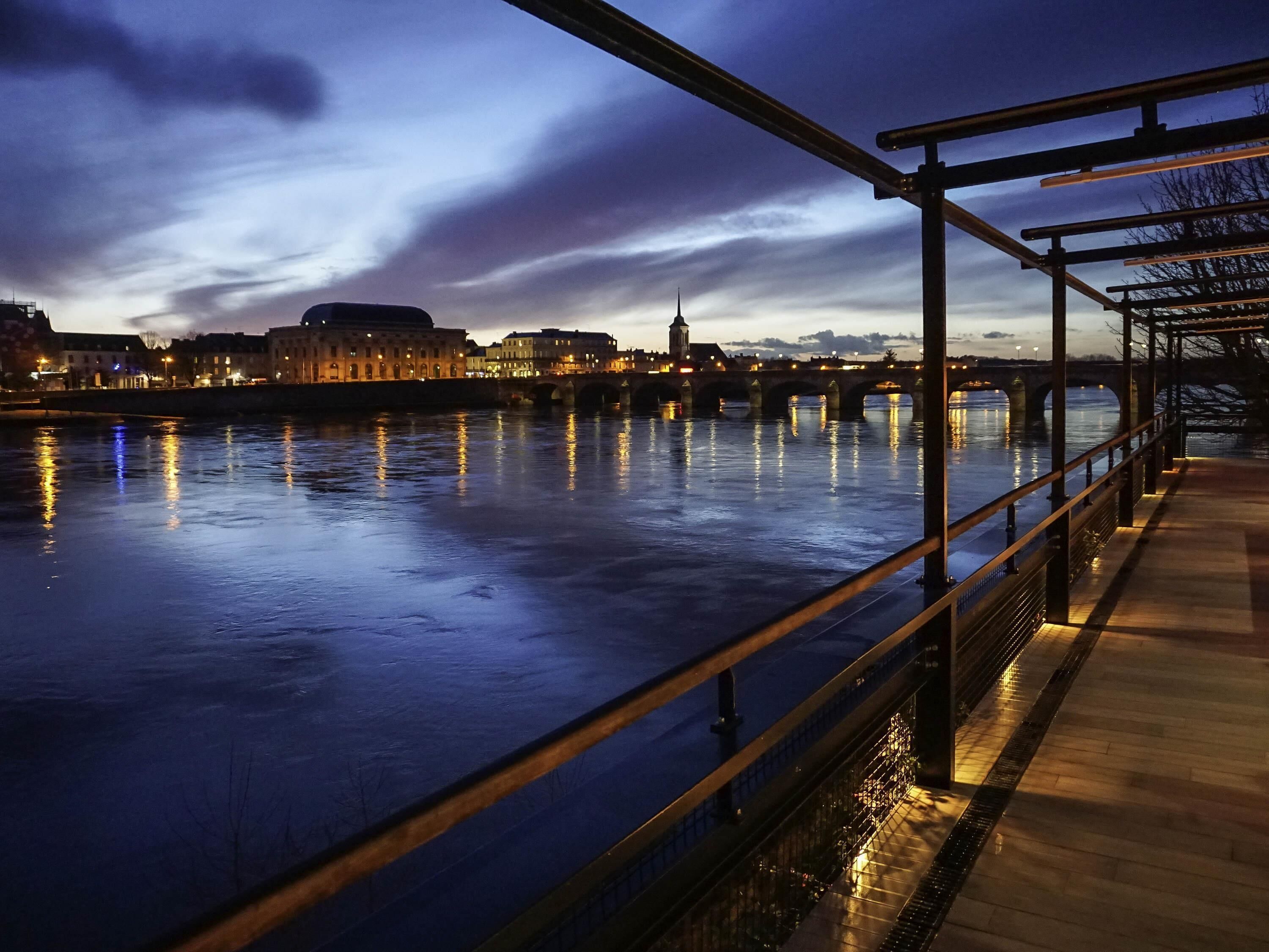 Vista nocturna de un río con un puente y edificios al fondo.