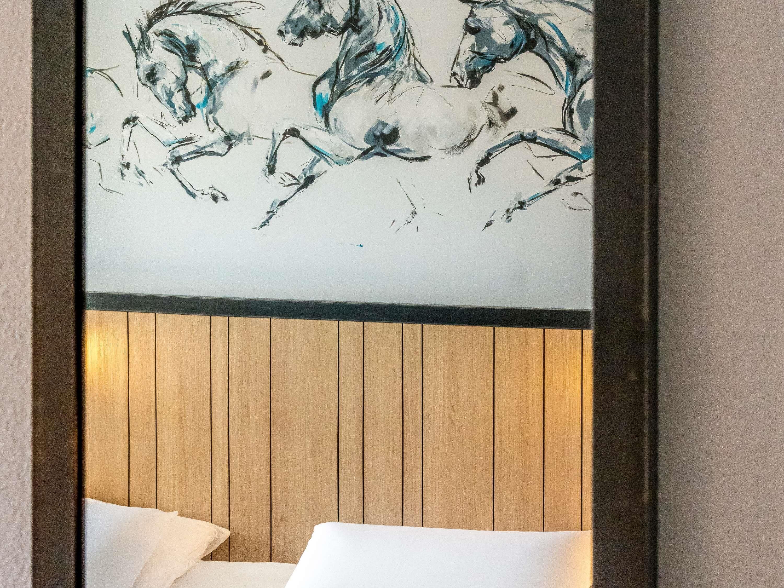 Ein Hotelzimmer mit einem hölzernen Kopfteil und einem großen, abstrakten Gemälde von Pferden.