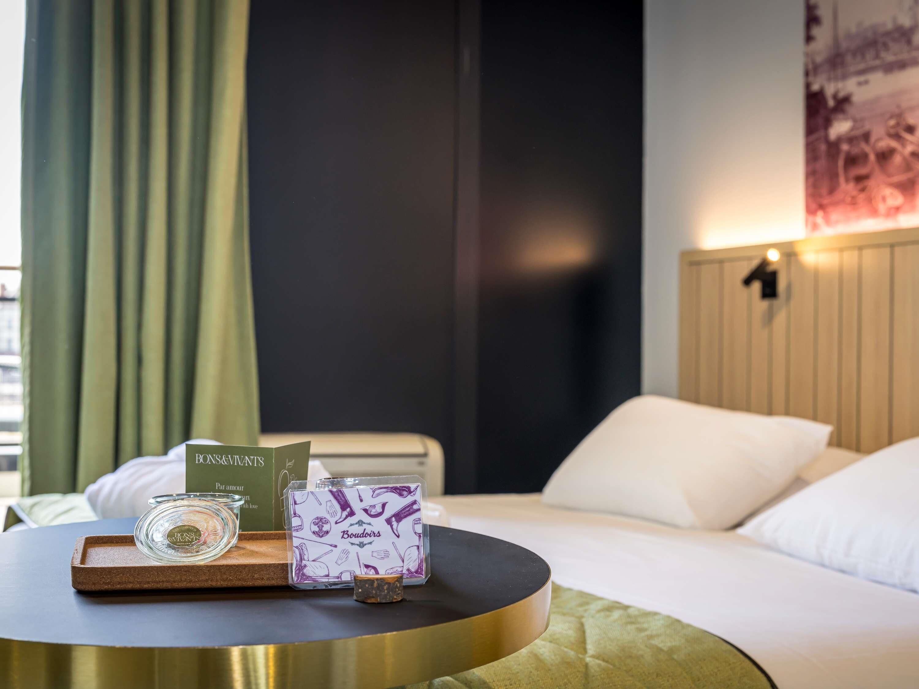 A hotel room with a bed, a round table with a tray, a glass, a box, and a card.