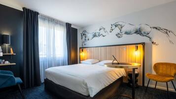 A hotel room with a bed, a desk with a laptop, a chair, a wall-mounted lamp, and a window with curtains.