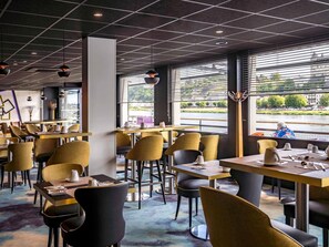 Een restaurant met tafels en stoelen, grote ramen en uitzicht op een rivier.
