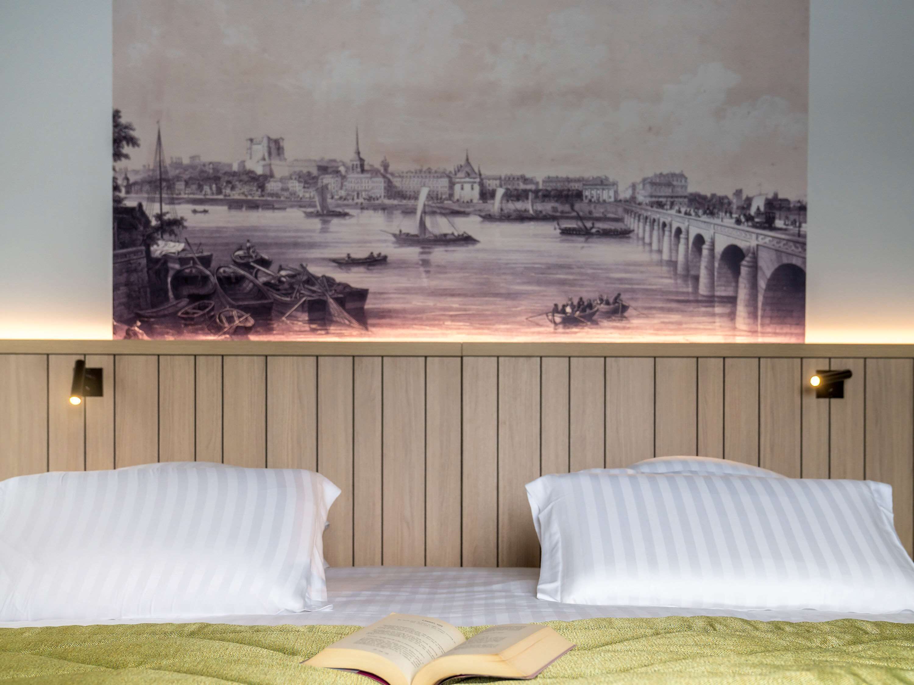 A bedroom with a bed, two pillows, a green blanket, and a wall-mounted painting of a riverside scene.