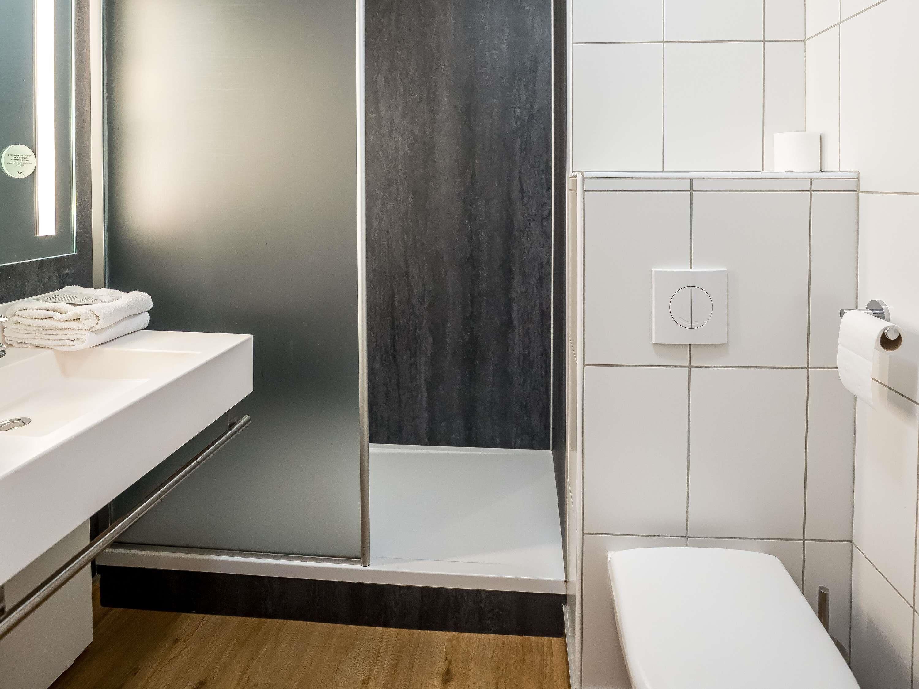 Een moderne badkamer met een wit wastafelmeubel, een douchecabine met glazen wanden en een toilet.