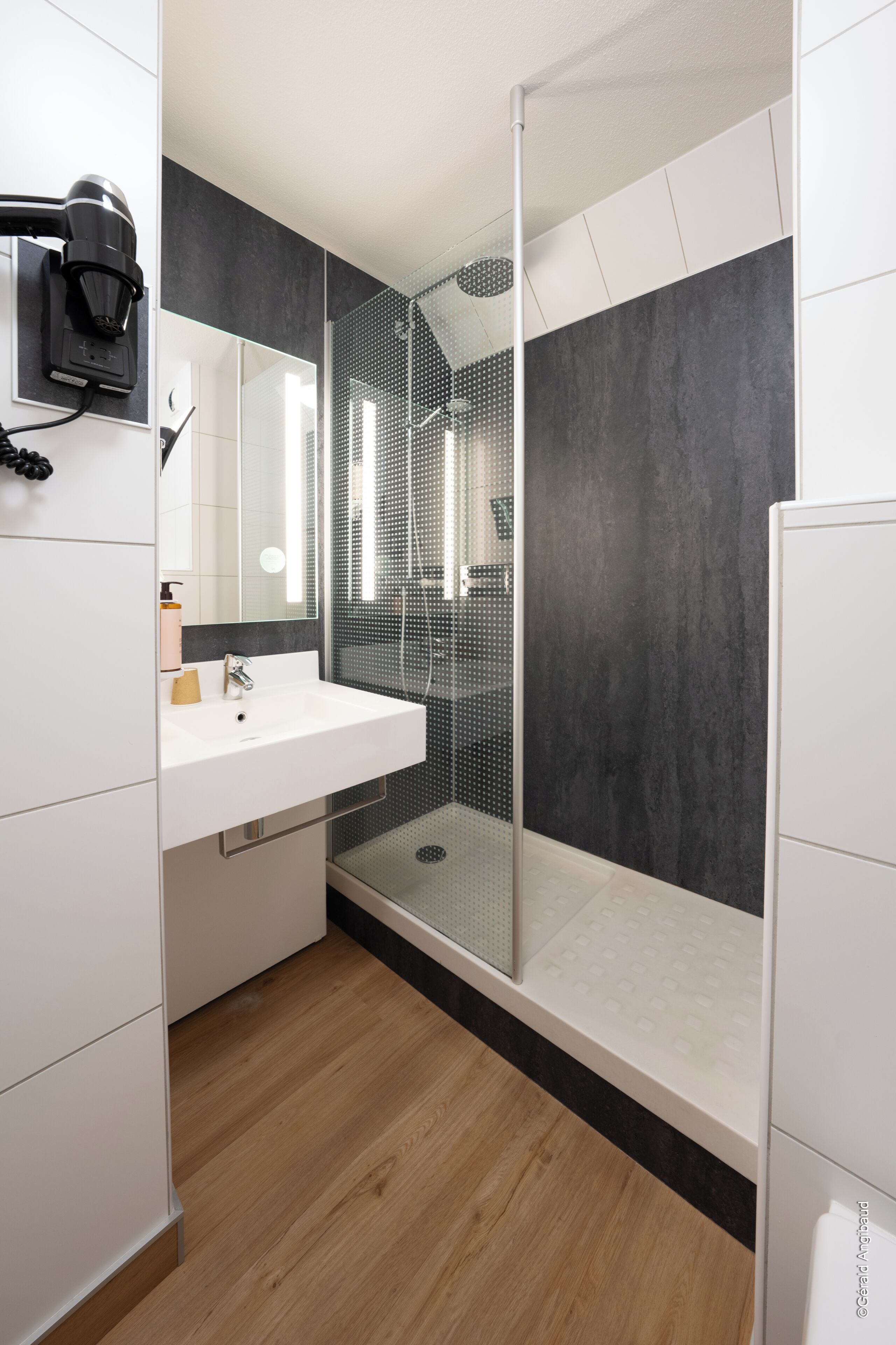 A modern bathroom with a glass shower enclosure, a white sink, and a mirror.