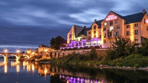 Un hotel con un puente al fondo, un reflejo en el agua y señalización iluminada.