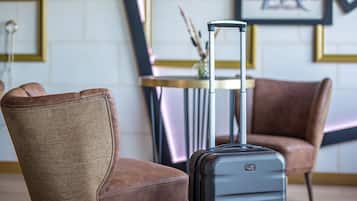 A hotel room with a brown leather chair, a black suitcase, and a table with a vase.