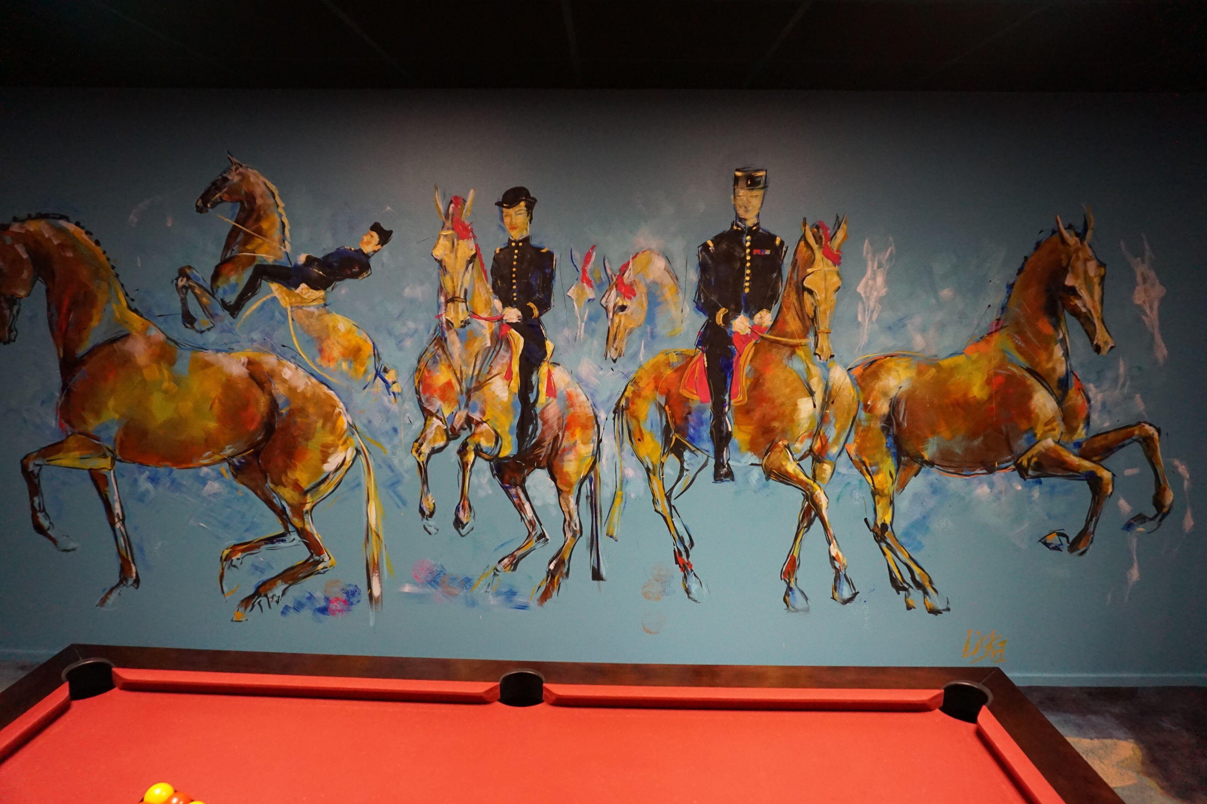 Una mesa de billar con un mural en la pared que representa caballos y jinetes.