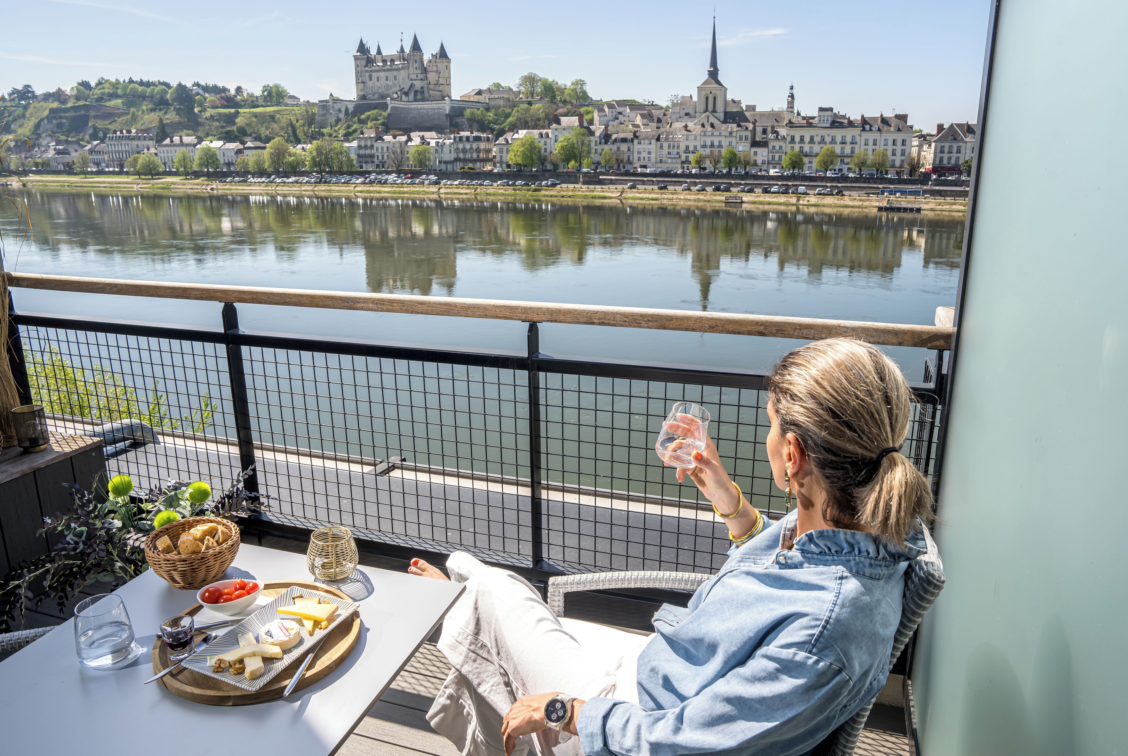 A balcony with a table set for a meal, overlooking a river with buildings in the background.