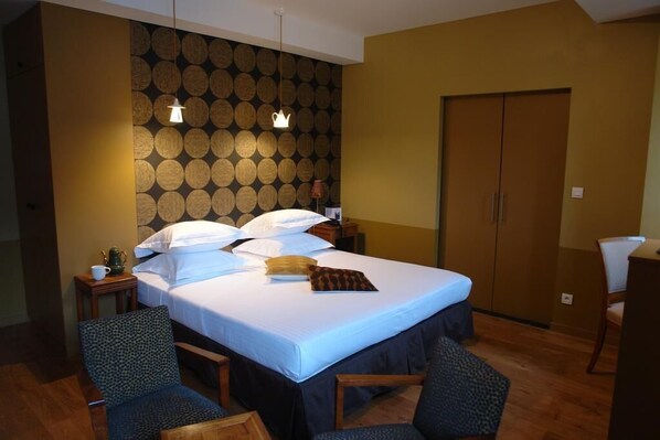 A hotel room with a large bed, two bedside tables, a wardrobe, and a seating area with two chairs.