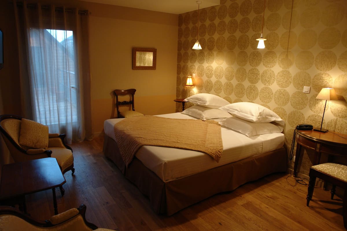A hotel room with a bed, two chairs, a desk, and a lamp.