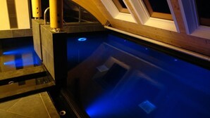 A modern indoor swimming pool with skylights and a sauna area.