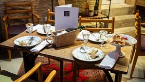 A dining table set with plates, cutlery, glasses, and a basket of wine bottles.