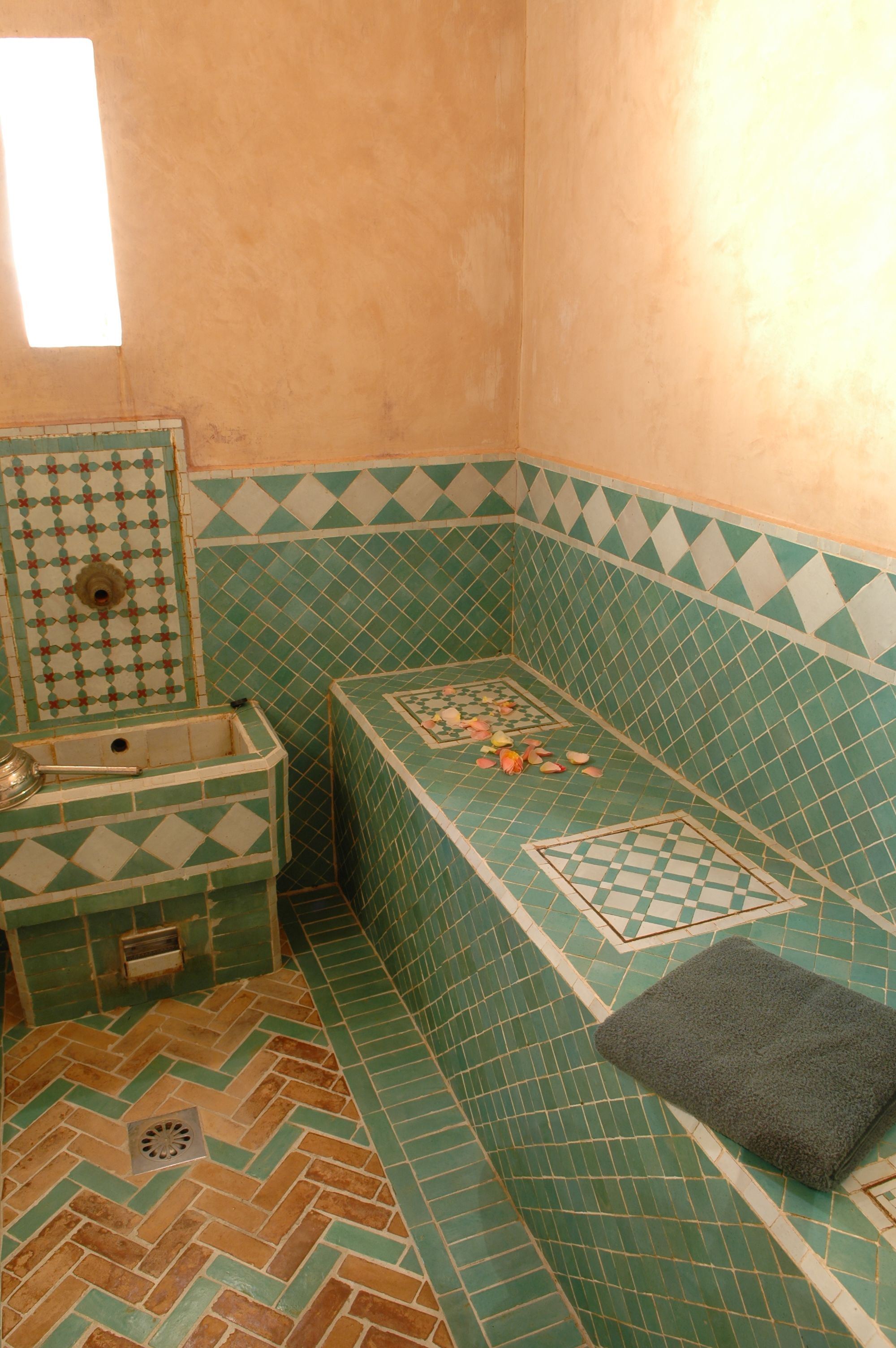 Une salle de bain avec un sol à motifs en chevrons, un lavabo agrémenté d’un miroir décoratif et un banc avec une serviette.